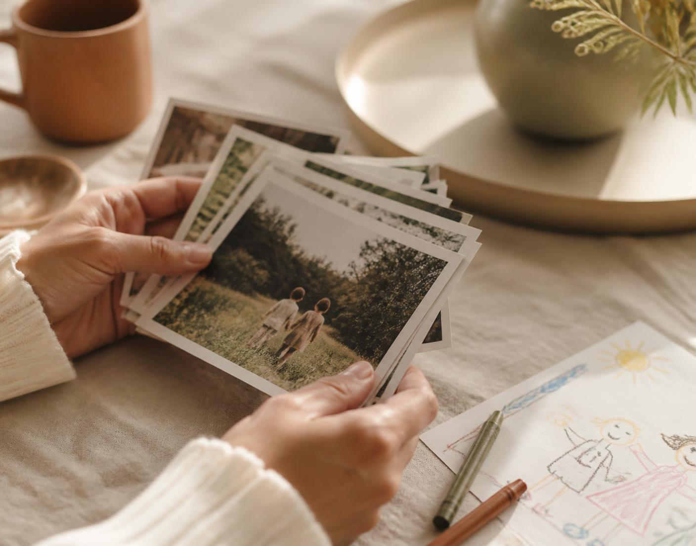 Des photos de famille imprimées posées sur une table en lin, à côté d'un dessin d'enfant
